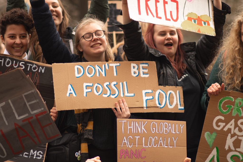 Youth gather holding signs in protest of fossil fuel. A youth centered in the photograph holds a sign that reads "Don't be a fossil fool"