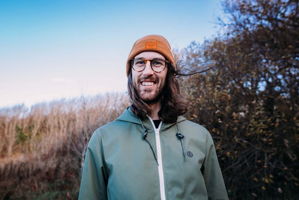 A photo of rust from the chest up. He is smiling and surrounded by brush and trees