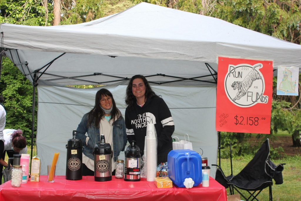 Two people stand side by side, smiling under an event tent. There is a sign that reads "Run for FUNds: You helped raise $2158.00" hanging from the tent 