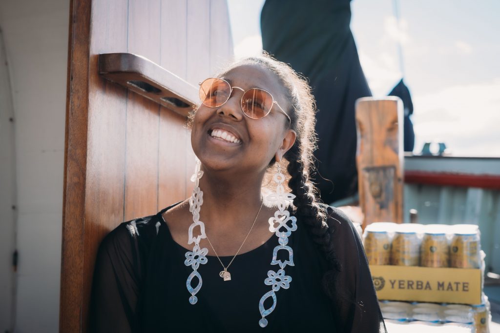 Desirée Dawson smiles on the deck of the Providence tall ship. In the background is a flat of Guayakí Yerba Mate