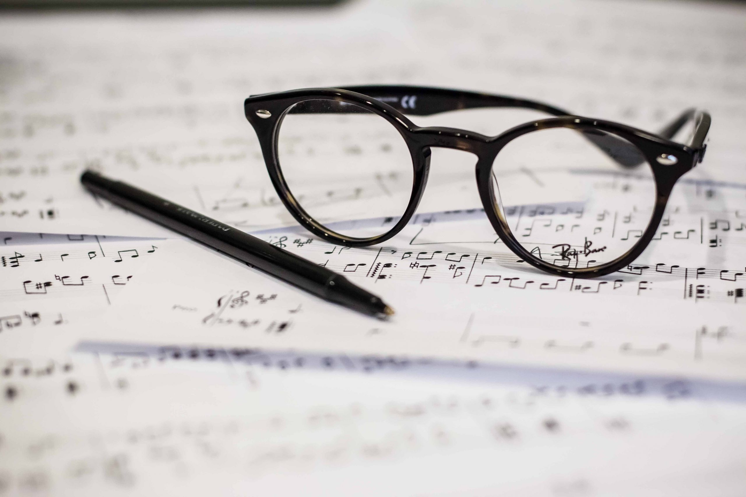close up of reading glasses and a pen on top of a messy pile of sheet music