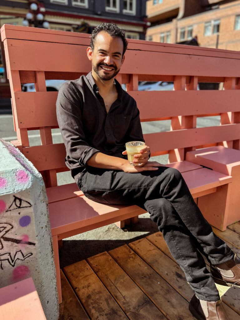 Gilberto sitting on a pink bench holding a cup of coffee