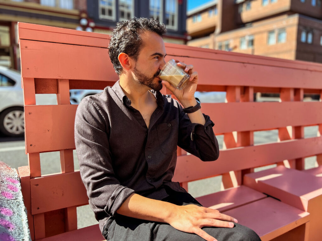 Gilberto sitting on a pink bench drinking a cup of coffee