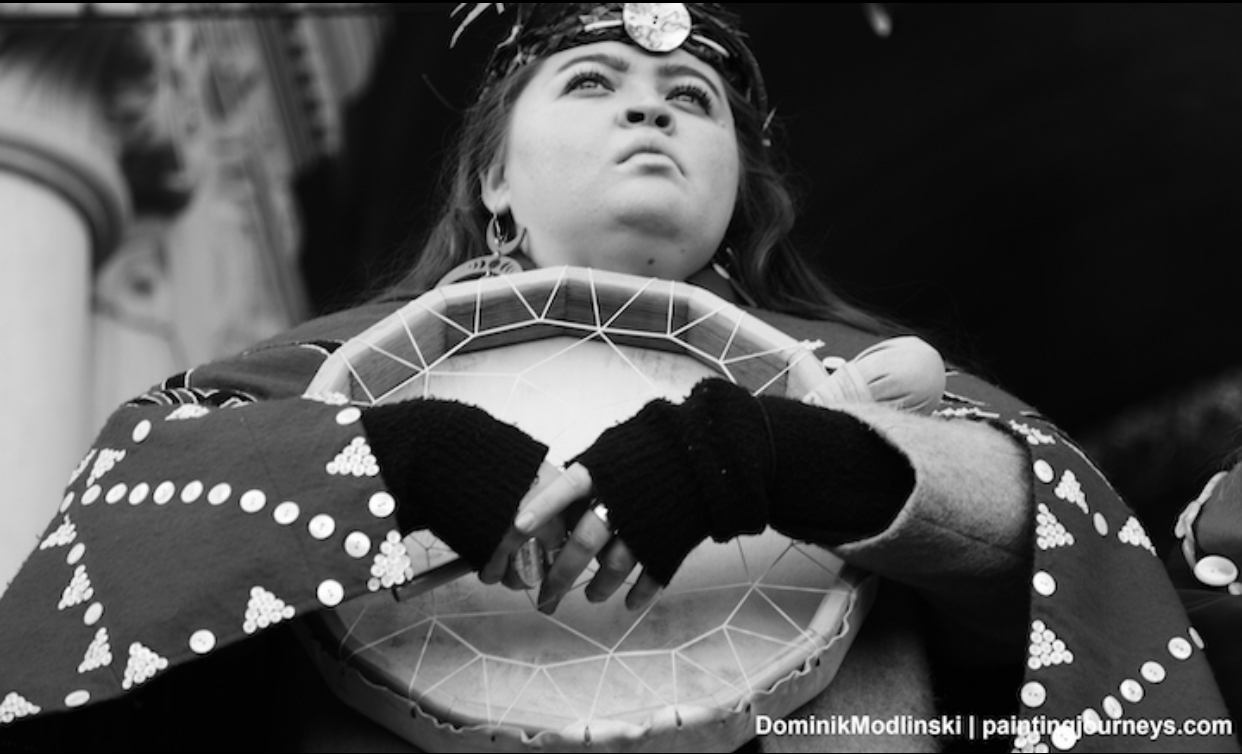 Black and white photo of a young Indigenous land protector holding drum